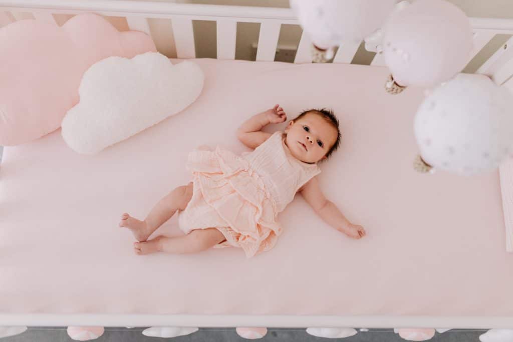 Newborn photo shoot in London-21 Baby girl is laying in her cot and looking at the camera. above her there are lovely balloons. London newborn photo session. Hampshire photography. Ewa Jones Photography