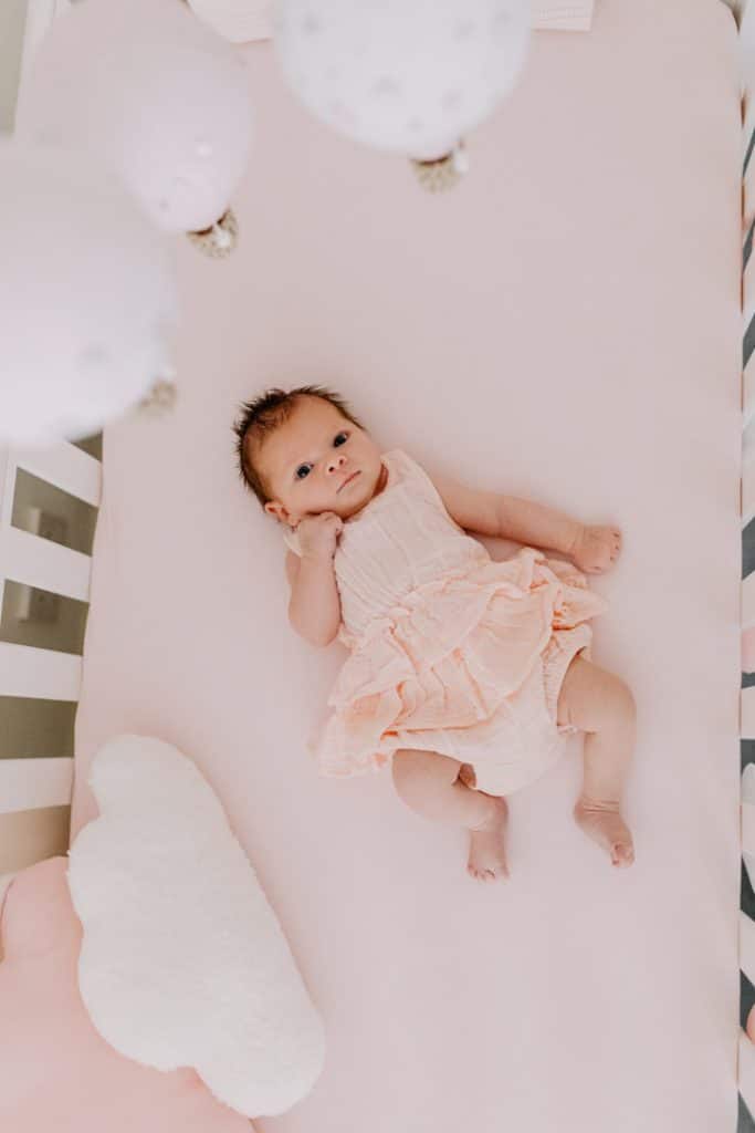 Newborn photo shoot in London-22 Baby girl is laying in her cot and looking at the camera. above her there are lovely balloons. London newborn photo session. Hampshire photography. Ewa Jones Photography
