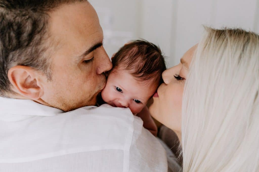 Newborn photo shoot in London-33 mum and dad are kissing their newborn baby girl. newborn baby photoshoot at home. Hampshire newborn photographer. Ewa Jones photography.