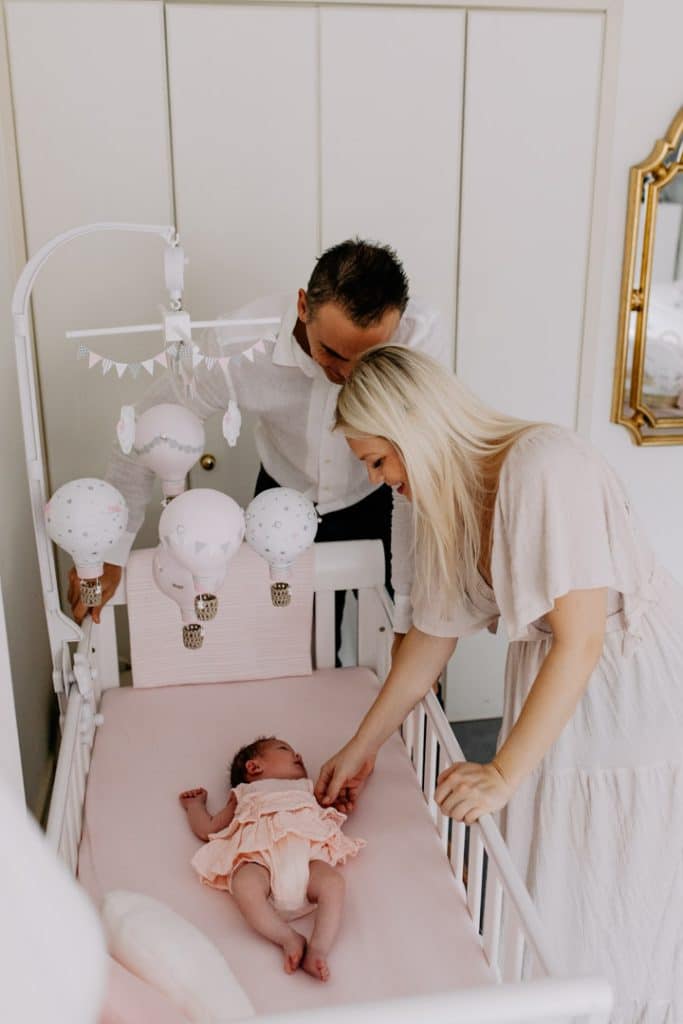 Newborn photo shoot in London-34 Mum and dad are standing next to baby girl cot and looking down at her. Lovely newborn photo session. Ewa Jones photography. Hampshire newborn photographer.