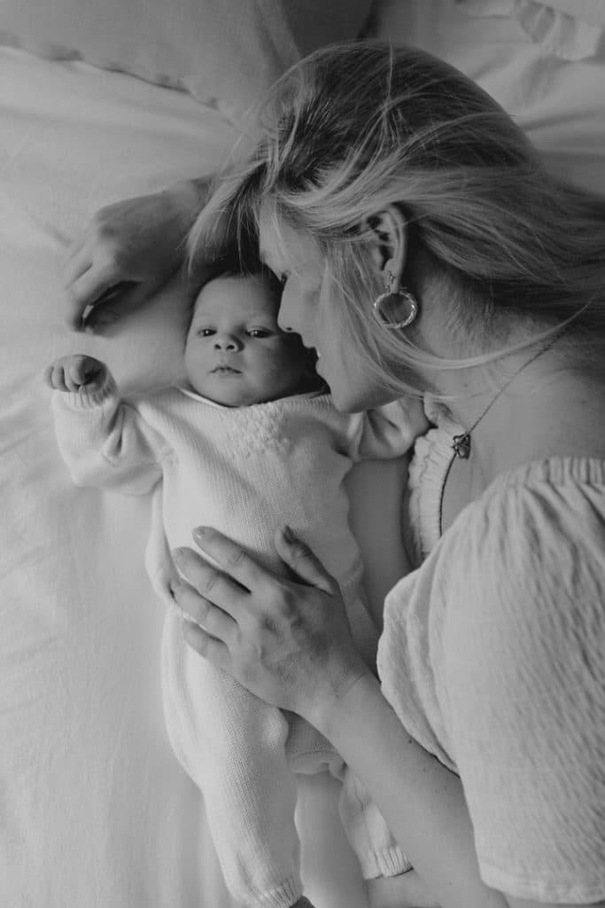 Newborn photo shoot in London-7 Mum is laying on the bed with her newborn baby girl Newborn baby girl is looking up. Newborn baby session at home. Basingstoke newborn baby photography. Ewa Jones Photography