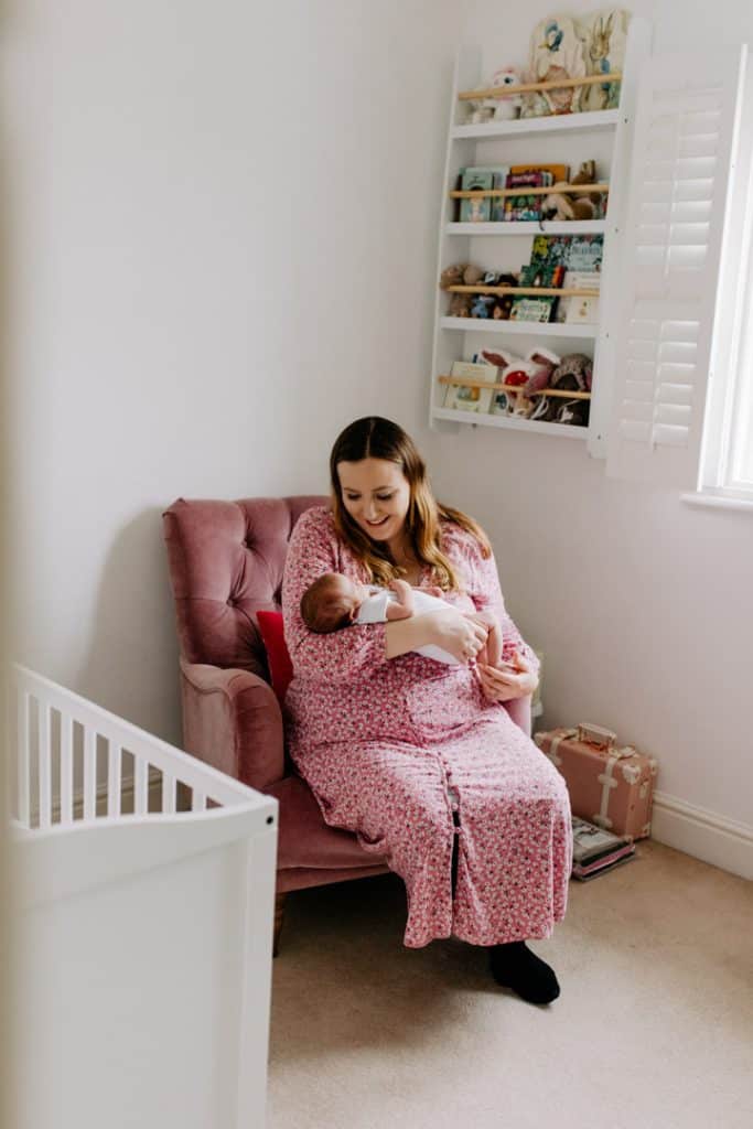 Mum is sitting on the newborn baby girl nursery on the chair and holding her newborn baby in her arms. Basingstoke photographer. Hampshire photographer. Ewa Jones Photography