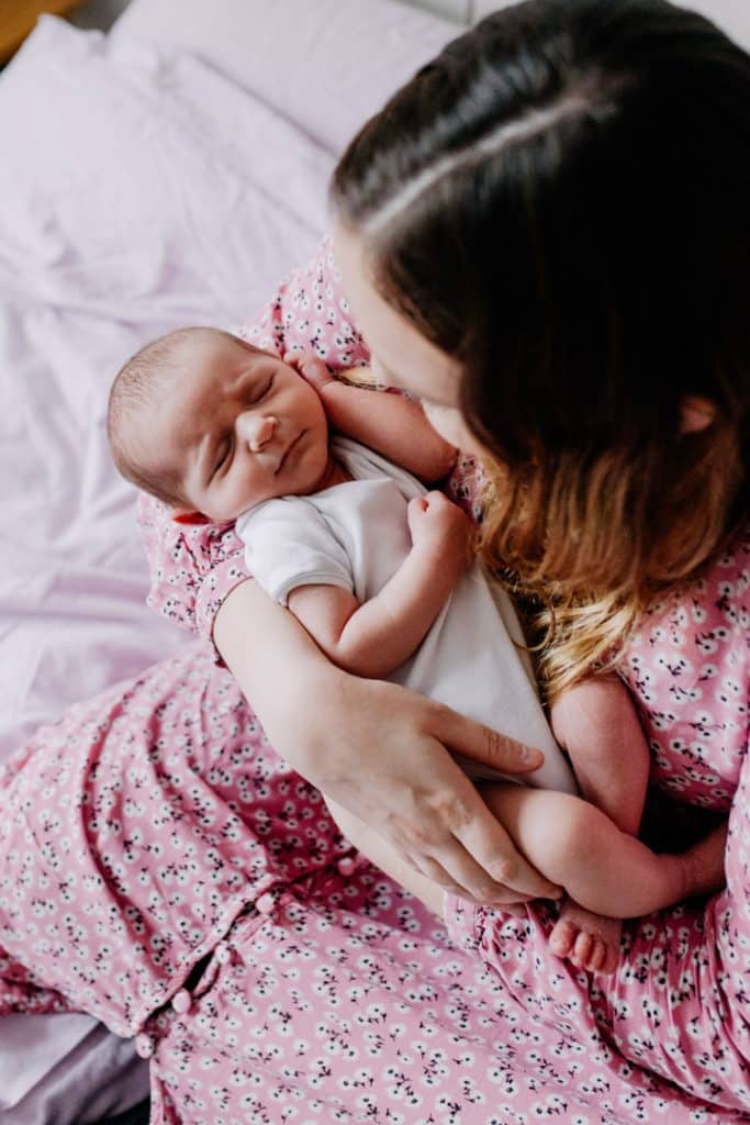 Mum is looking down at her newborn baby girl. Mum is sitting on the bed. Newborn baby girl is sleeping. Lifestyle newborn photo session. Hampshire newborn photography. Ewa Jones Photography
