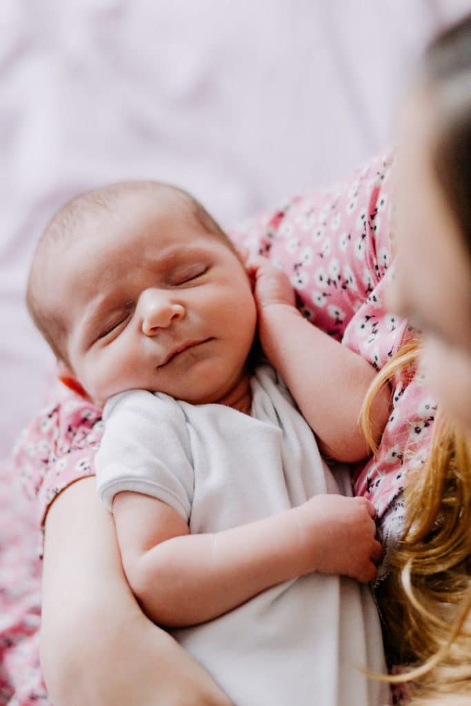 Mum is looking down at her newborn baby girl. Mum is sitting on the bed. Newborn baby girl is sleeping. Lifestyle newborn photo session. Hampshire newborn photography. Ewa Jones Photography. Basingstoke photography