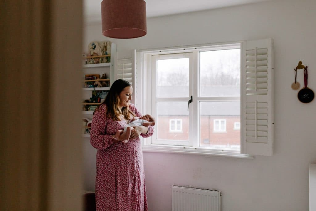 Mum is standing in newborn baby nursery and holding her newborn baby. Lovely natural newborn baby photo session at home. Hampshire newborn photographer. Ewa Jones Photography