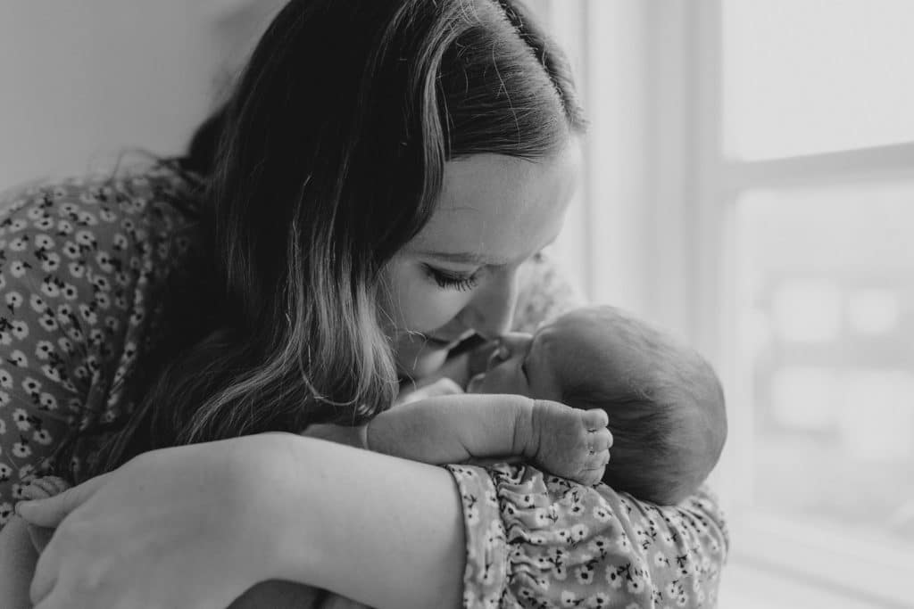 Black and white image of mum cuddling her newborn baby girl. she is touching her newborn baby nose with her nose. Newborn photoshoot in Hampshire. Ewa Jones Photography. Newborn photography in Basingstoke - first days