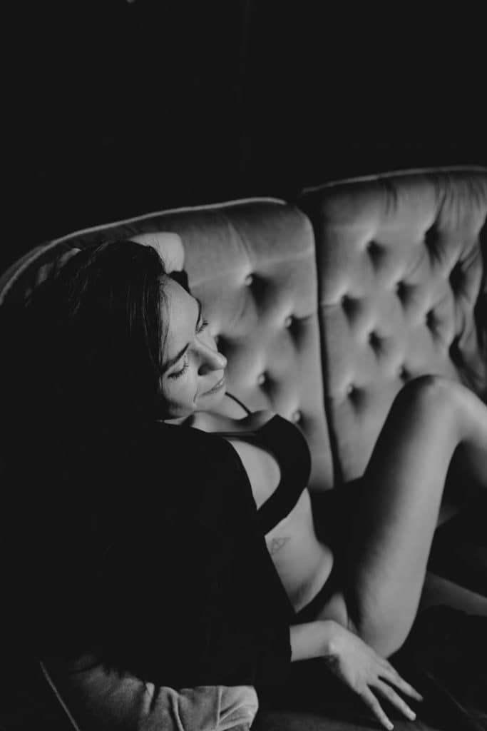 Female is sitting on the sofa and looking down. Boudoir female photo session in Hampshire. Ewa Jones Photography
