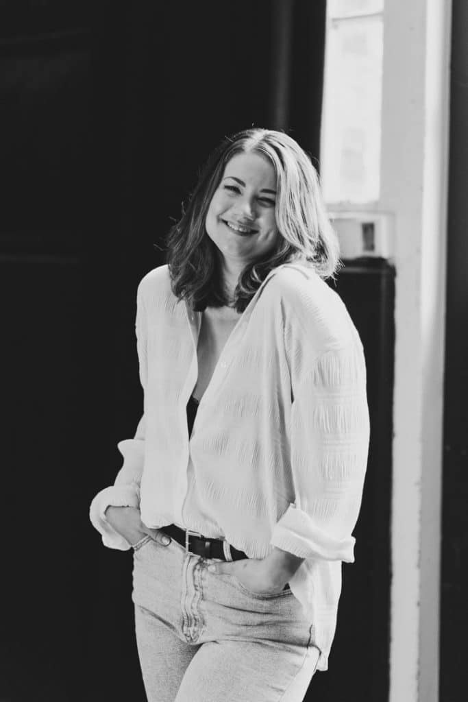 Female is standing and looking at the camera. She is smiling and wearing jeans and white shirt. Female photo sessions in Hampshire. Empowering female sessions. Ewa Jones Photography