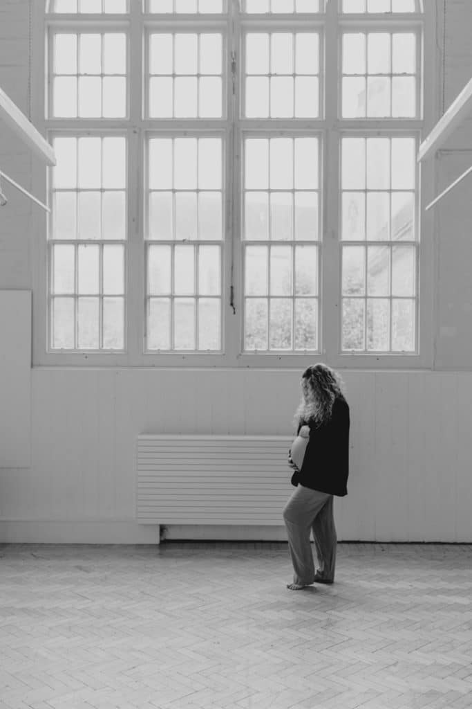 Female is looking down at her bump. Hampshire maternity photo session in the studio. Ewa Jones Photography