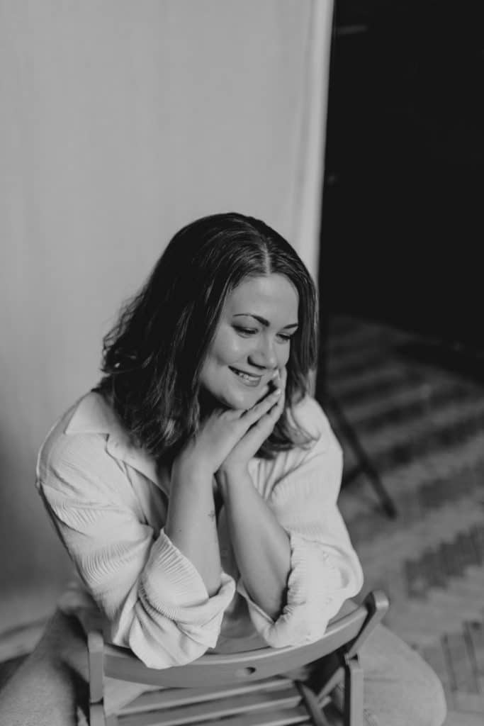 Female is sitting on the chair and looking down. she is smiling. Empowering female photo sessions. Positivity in female photography. Ewa Jones Photography