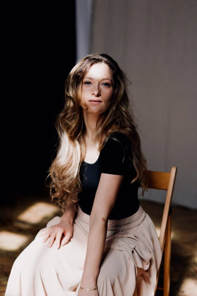 Female is sitting on the chair and looking at the lens. She is wearing black top and wide trousers. Female photo shoot in Basingstoke. Ewa Jones Photography
