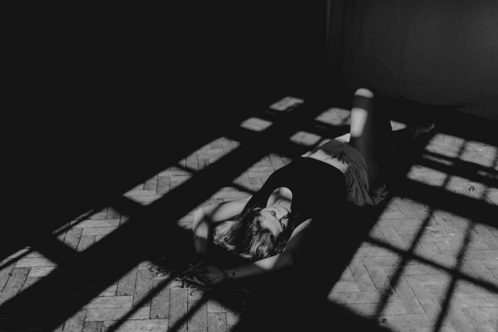 Female is laying on the floor and the sun shadows are on her body. Empowering female sessions. The journey of self-love through empowering female photo sessions Part 1. Ewa Jones Photography
