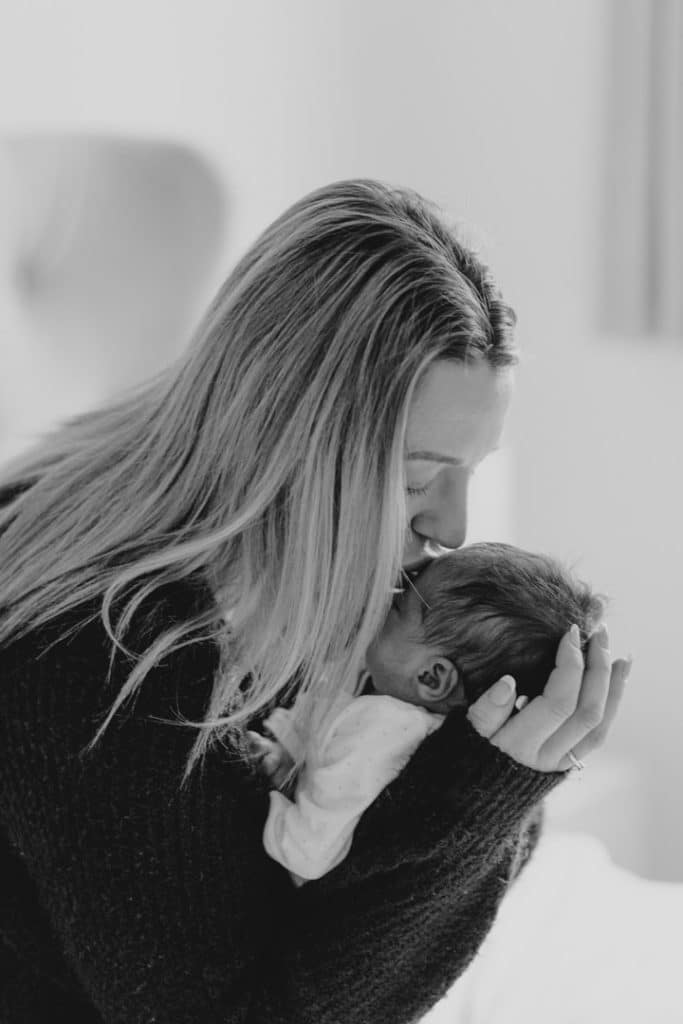 Mum is kissing her newborn baby girl on top of her head. Natural in home newborn photo sessions. Hampshire photographer. Ewa Jones Photography