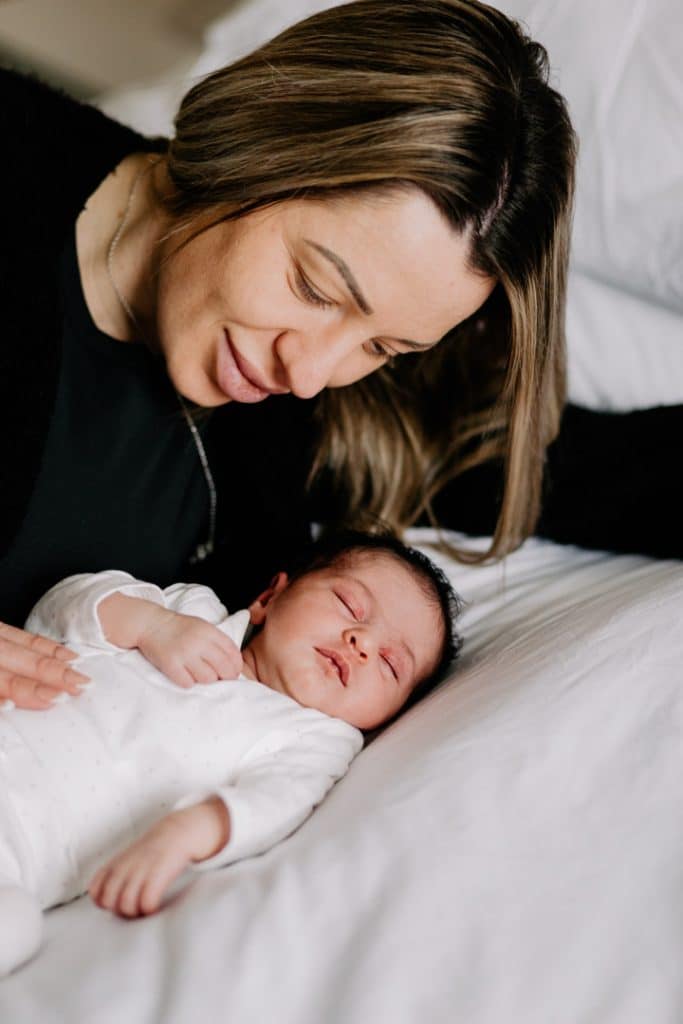 mum is looking down at her newborn baby girl. baby girl is sleeping on the bed. Hampshire newborn photo session. Ewa Jones Photographer