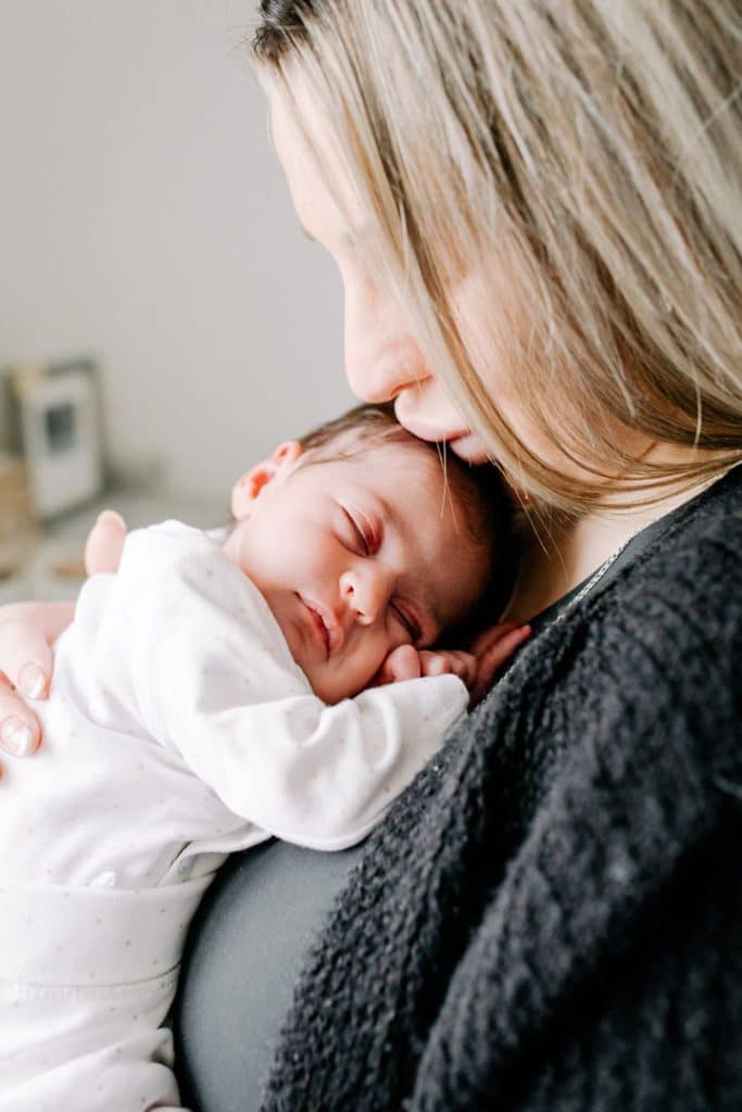 Mum is holding her newborn baby girl and she is sleeping in mummy's arms. Candid newborn photo shoot in Hampshire. Ewa Jones Photography