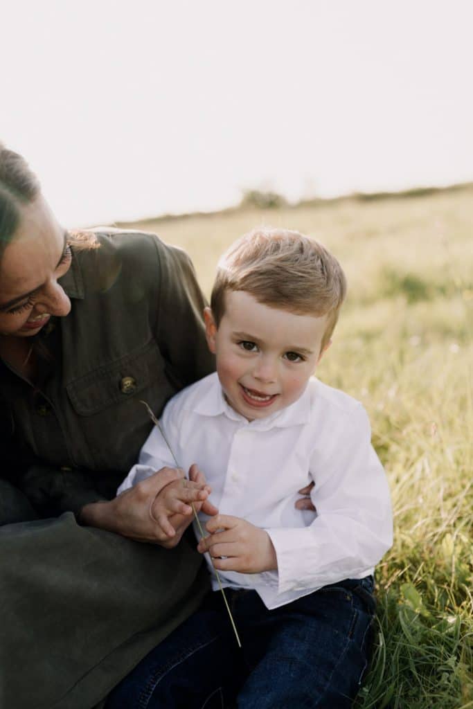 Claudia and Lorenzo-14 boy is sitting on the grass and looking at the camera. Mum and son photo session in Spring time. What to wear for family photo session. Hampshire family photographer. Ewa Jones Photography
