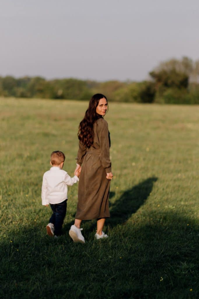Claudia and Lorenzo-19 Mum is walking with her son and looking back at the camera. lovely green field with sunset. Family photo shoot in Hampshire. Basingstoke photographer. Ewa Jones Photography