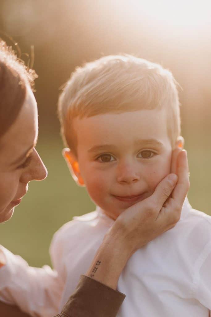 Claudia and Lorenzo-21 Mum is holding her hand on her little boy face. little boy is looking directly at the camera. Lovely natural image with sun at the back. Sunset photo session. Family photo session in Hampshire. Hampshire photographer. Ewa Jones Photography