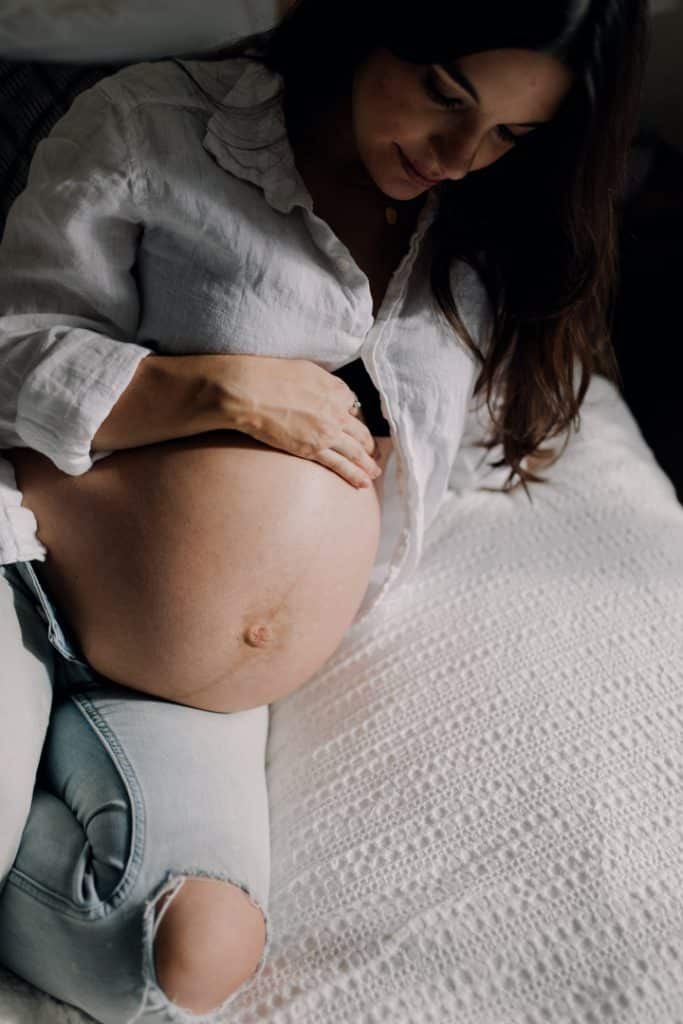 mum is sitting on bed and looking down at her baby bump. maternity photo session at home. Maternity photographer in Hampshire. Maternity photoshoot in Hampshire. Ewa Jones Photography