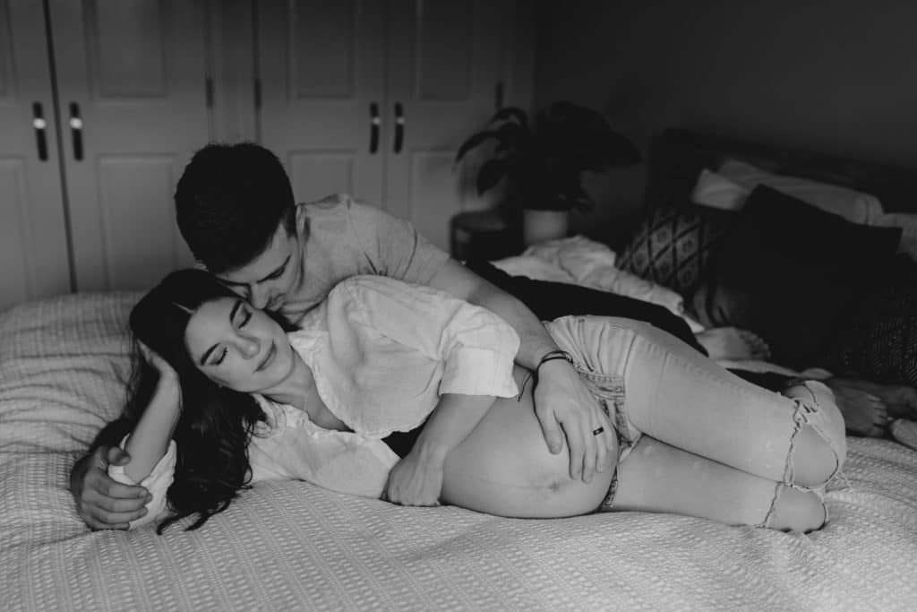 Mum and dad are laying on bed and being close with each other. Maternity photo shoot at home. Maternity photo session in Hampshire. Hampshire photographer. Ewa Jones Photography
