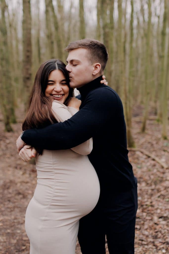 Dad is kissing mum to be on her head. Maternity photo session outside. What to wear for maternity session. Hampshire photographer. Hampshire maternity photo sessions. Ewa Jones Photography