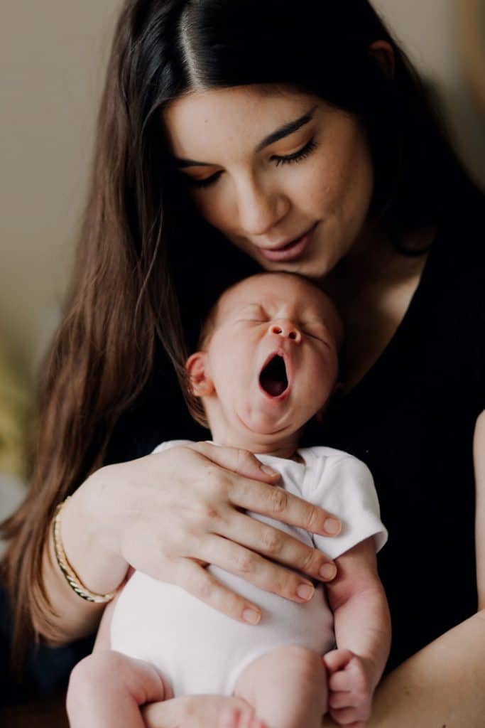 newborn baby is yawning. mum is holding the baby. mum is wearing black and baby is in the white vest. Newborn photo session in Hampshire. Hampshire photographer. Ewa Jones Photography