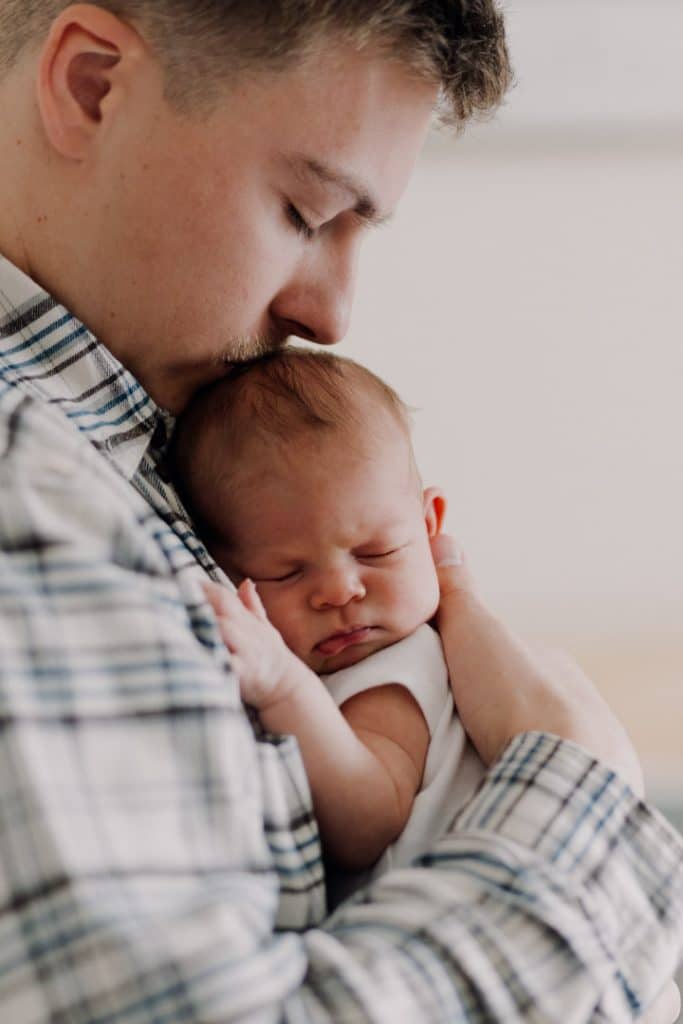 dad is holding close his baby girl and kissing on her head. lovely candid moment of dad and newborn baby. Newborn photo shoot at home. Hampshire photographer. Ewa Jones Photography
