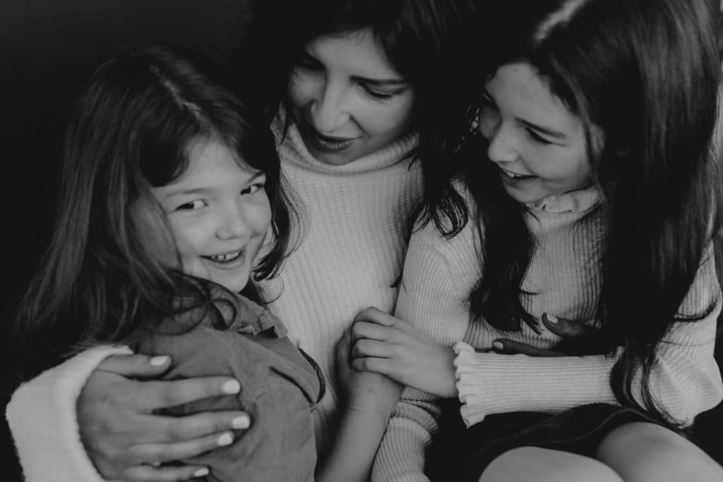 Mum is cuddling her two girls and looking at one. One girls is looking at the camera. Lovely family photo shoot in Hampshire. Hampshire family photographer. What to wear for family photo session. Ewa Jones Photography