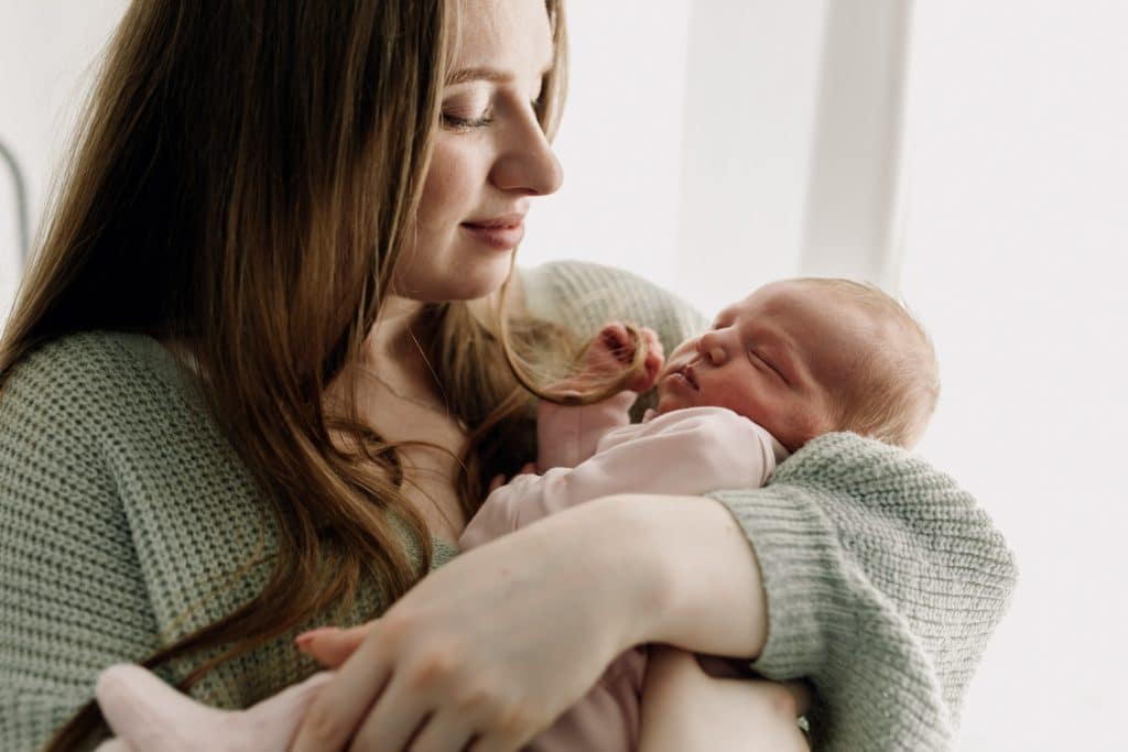 Mum is holding her newborn baby girl in her arms, Newborn baby is sleeping. Lovely in home newborn photo session. Newborn photographer in Hampshire. Newborn photographer in Basingstoke. Hampshire photographer. Ewa Jones Photography