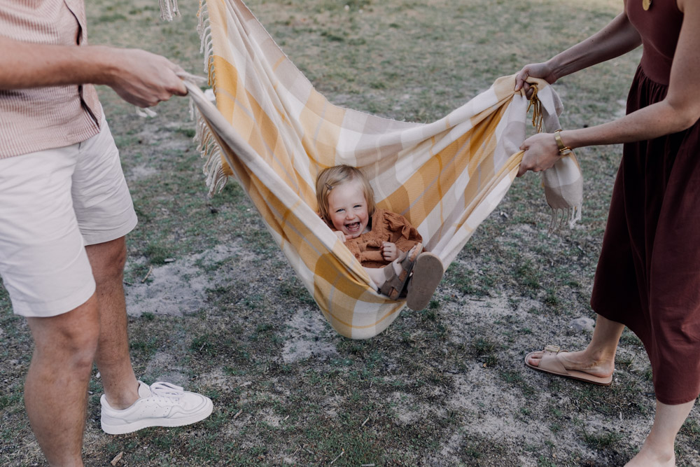 Little girl is inside the blanket and mum and dad are swinging her. she is laughing. family photographer in Hampshire. Ewa Jones Photography