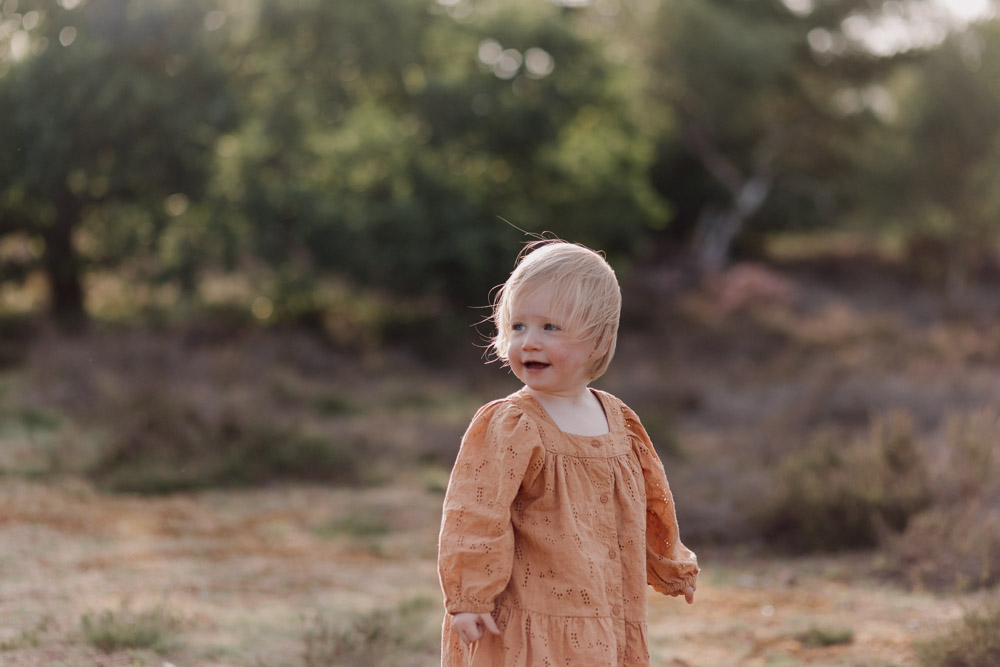 little girl is looking and smiling. she is wearing lovely orange dress. family photographer in Basingsoke. Ewa Jones Photography