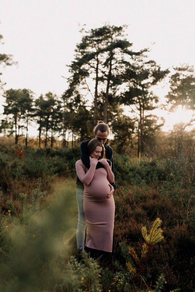 Maternity photo session in Basingstoke 06.12.24-7 lovely expecting parents are hugging close. natural common surrounds them. Sun is shining and there is lots of trees. Maternity photo session in Hampshire. Ewa Jones Photography