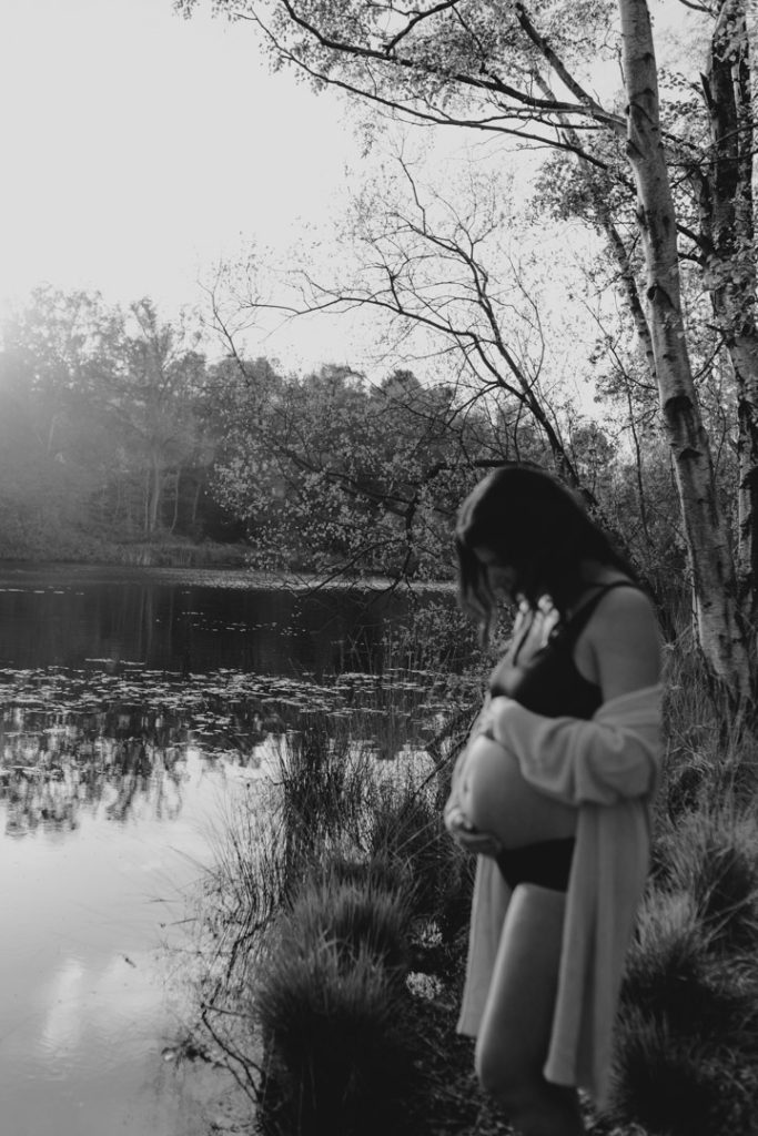 Mum is looking down at her bump. Lovely scenery. Nature reserve. Pond in the background. Ewa Jones Photography