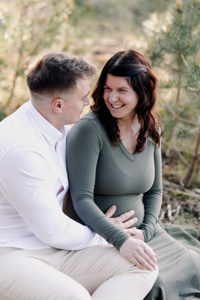 Mum and dad are smiling and sitting on the blanket. outdoor maternity session in Hampshire. Hampshire maternity photographer. Ewa Jones Photography