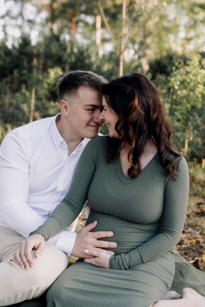 Mum and dad are smiling and sitting on the blanket. outdoor maternity session in Hampshire. Hampshire maternity photographer. Ewa Jones Photography