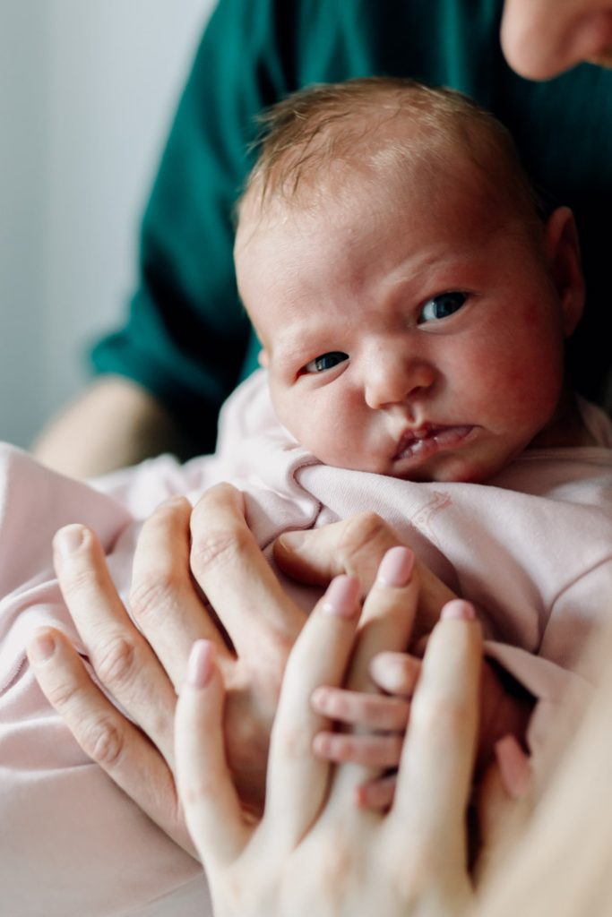Newborn photo session in Basingstoke 19.01.24-3 Newborn baby is looking at the camera. Baby is wearing pink body suit. Hampshire newborn photo session at home. Ewa Jones Photography