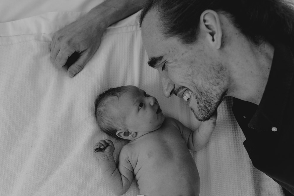 Newborn photo session in Basingstoke 19.01.24-6 dad is laying on the bed and looking down at the baby. Newborn shoot at home. Ewa Jones Photography