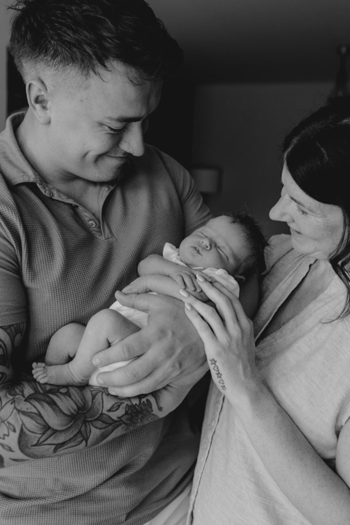 Lovely happy image of mum dad and baby girl. dad is holding baby girl in his hands. newborn session in Hampshire. Ewa Jones Photography