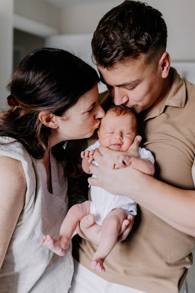 Mum and dad are kissing their newborn baby. Newborn photo shoot. Hampshire newborn photographer. Ewa Jones Photography