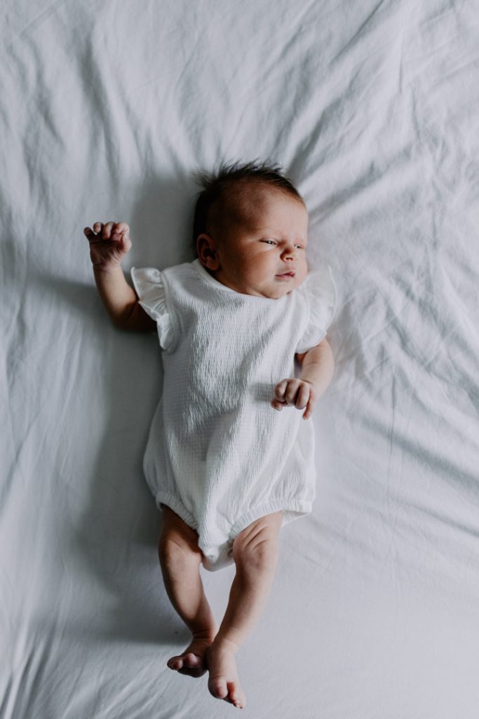 Baby girl is laying on bed and looking up. lovely in home lifestyle photo session. Ewa Jones Photography