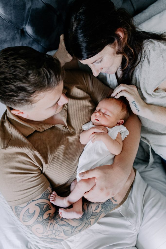 mum and dad are laying on bed and looking down at their baby girl. Natural photo session in home. Ewa Jones Photography