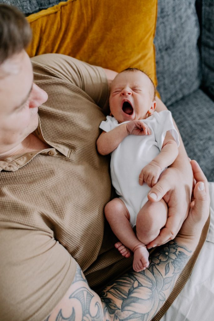 Newborn baby girl is yawning. she is being held by her dad. newborn photo session in Hampshire. Baby girl is in her baby crib. in home newborn photo session. Hampshire newborn photo shoot. Ewa Jones Photography