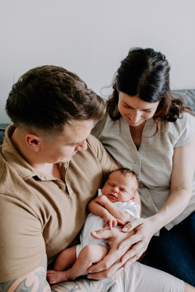 Lovely happy image of mum dad and baby girl. dad is holding baby girl in his hands. newborn session in Hampshire. Ewa Jones Photography
