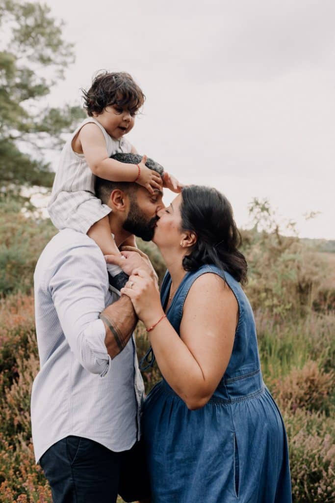 Mum and dad are giving each other a kiss. their boy is on dad's shoulders. Family lovely fun time. Ewa Jones Photography