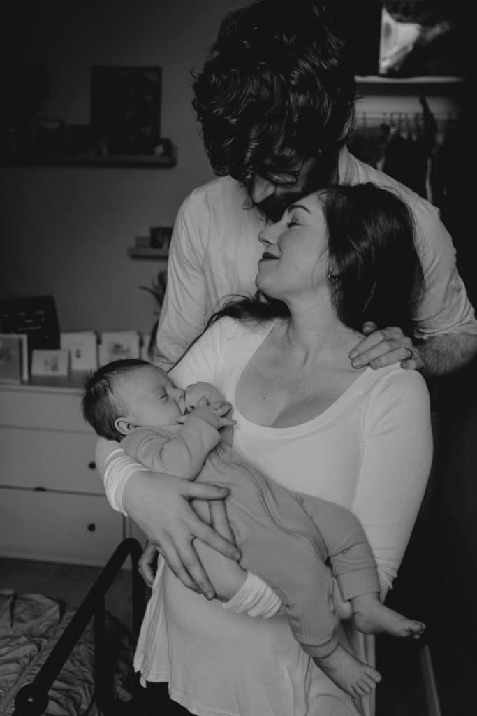 Mum is holding her baby boy and feeling happy. dad is standing behind and looking down at his baby boy. Hampshire newborn photoshoot. Hampshire photographer. Ewa Jones Photography