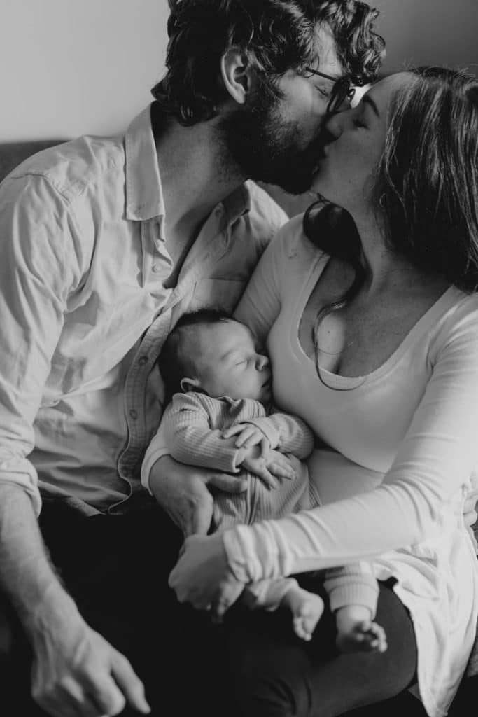 Mum and dad are kissing and holding their baby boy in their arms. London newborn photo shoot at home. Hampshire newborn photographer. Ewa Jones Photography