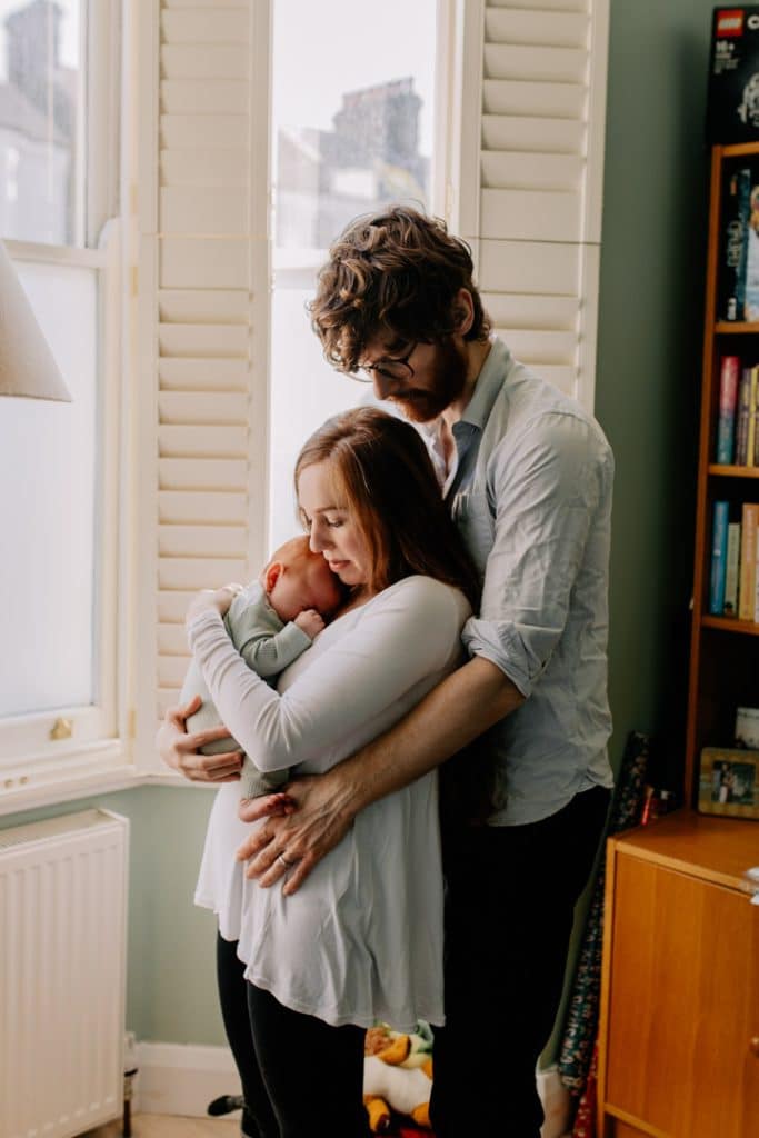 Mum and dad cuddling and holding baby boy. Baby by is sleeping in mums arms. in home newborn photo shoot. Newborn photo session. Hampshire photographer. Ewa Jones Photography
