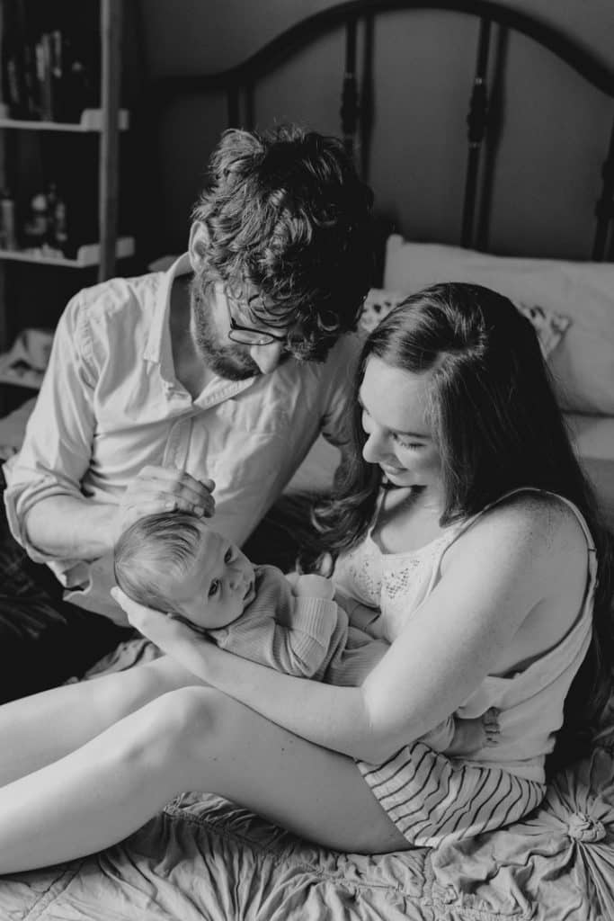 mum and dad are sitting on the bed and looking at their baby boy. intimate newborn photosession. Ewa Jones Photographer