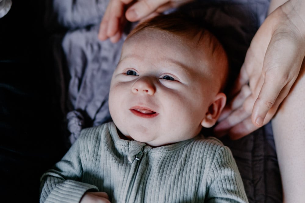 Baby boy is looking up and smiling. Newborn photo session. In home newborn photo shoot. Ewa Jones Photographer