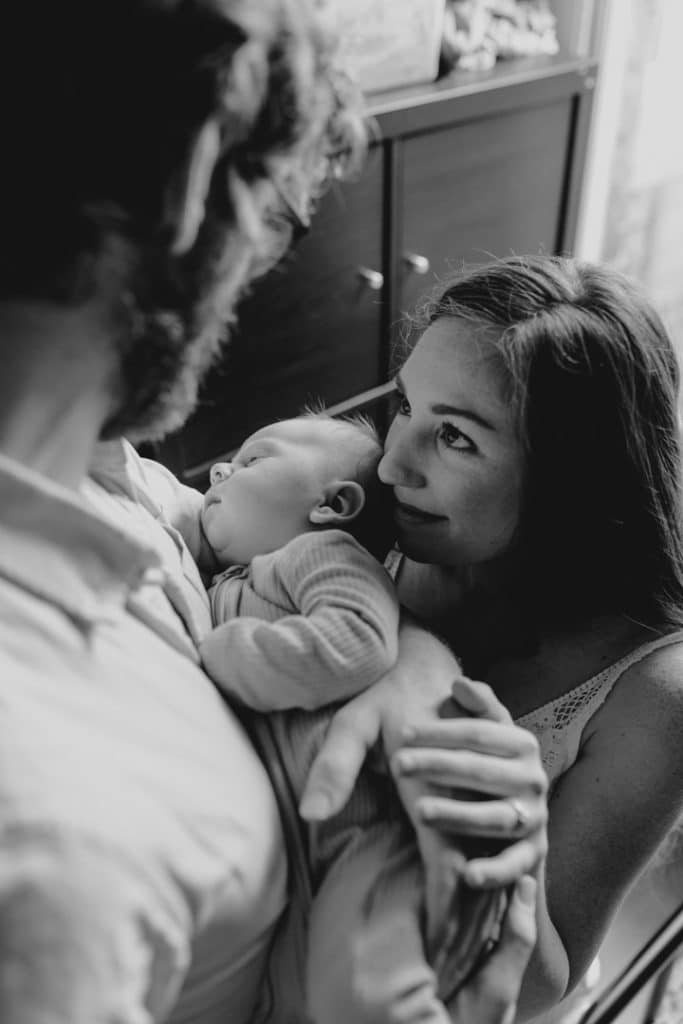 Mum is cuddling to her baby son and looking at her husband. Newborn photoshoot in Hampshire. Ewa Jones Photography
